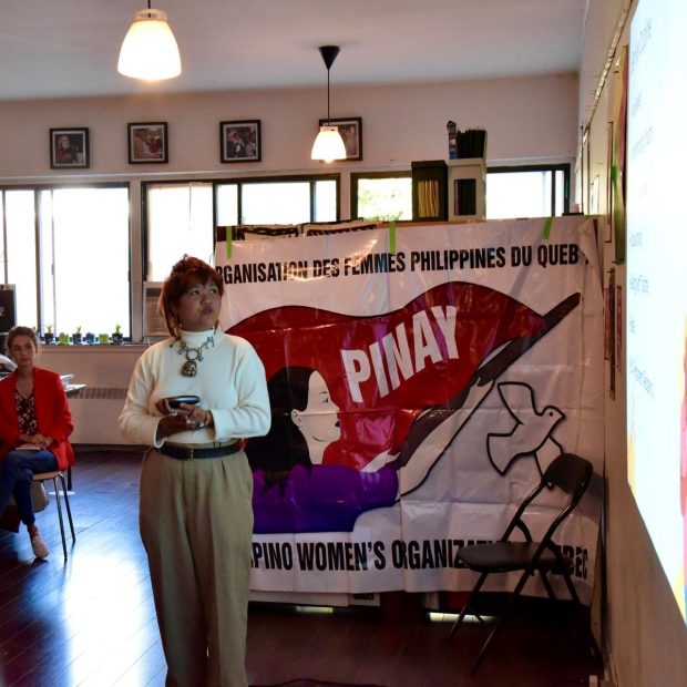 A photograph of an individual giving a presentation in front of a PINAY Quebec banner.