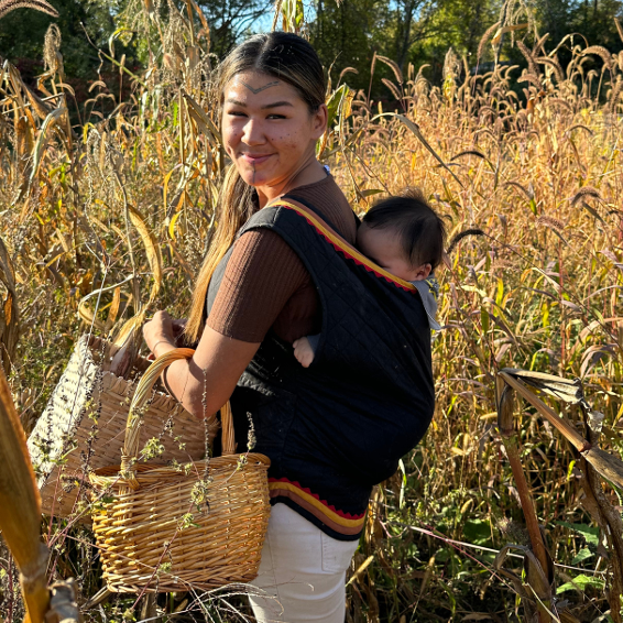 Photo of an Inuit woman in a corn field with a baby on her back