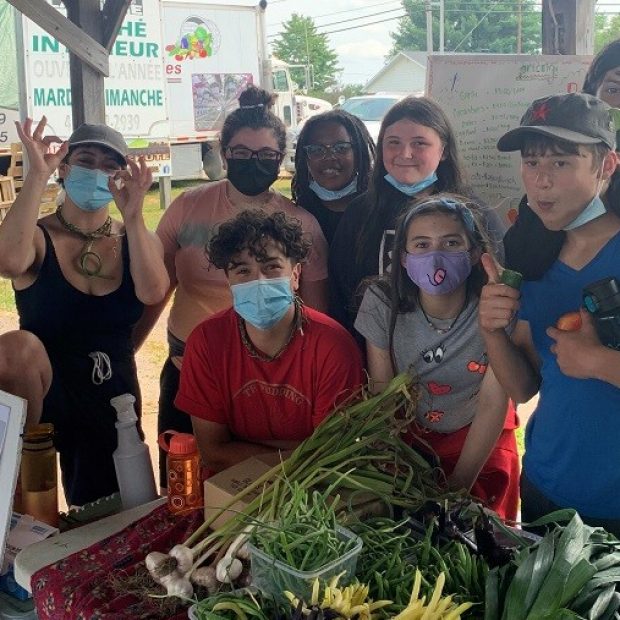 A photograph of a group of youth posing in front of harvest vegetables.