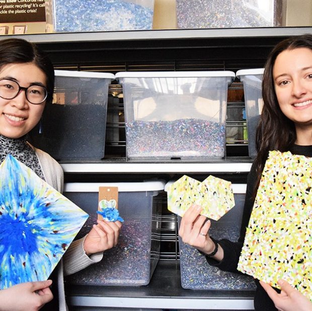 A photograph of two individuals holding up earrings and coasters made from recycled plastics.