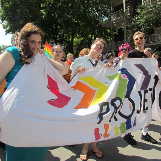 A photograph of three people holding a Project 10 banner during a march.