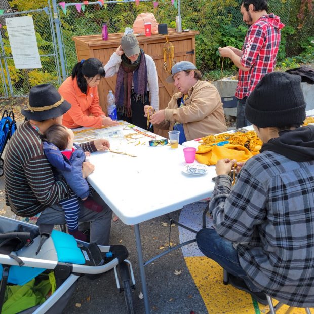 A photograph of a small group of people doing arts projects on a table outside.