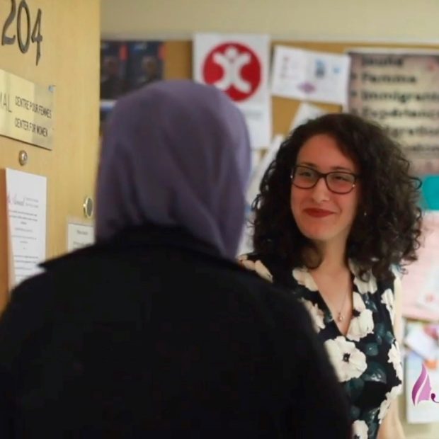 A woman welcomes another woman in a hijab into her office.