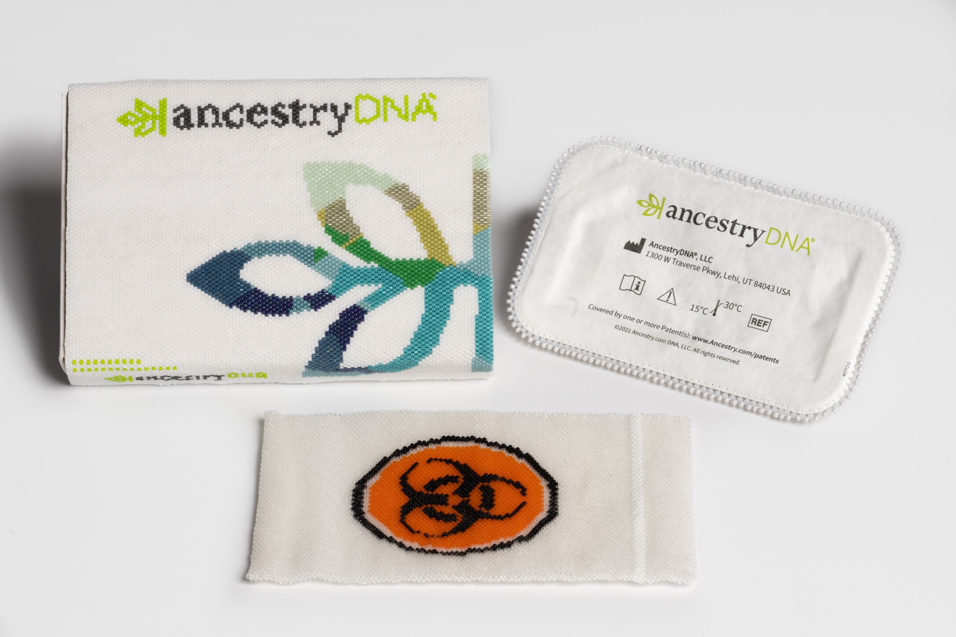 A beaded white box and a beaded white pill tablet, both with the text "ancestry DNA", with a beaded pouch displaying the orange symbol for biohazard.