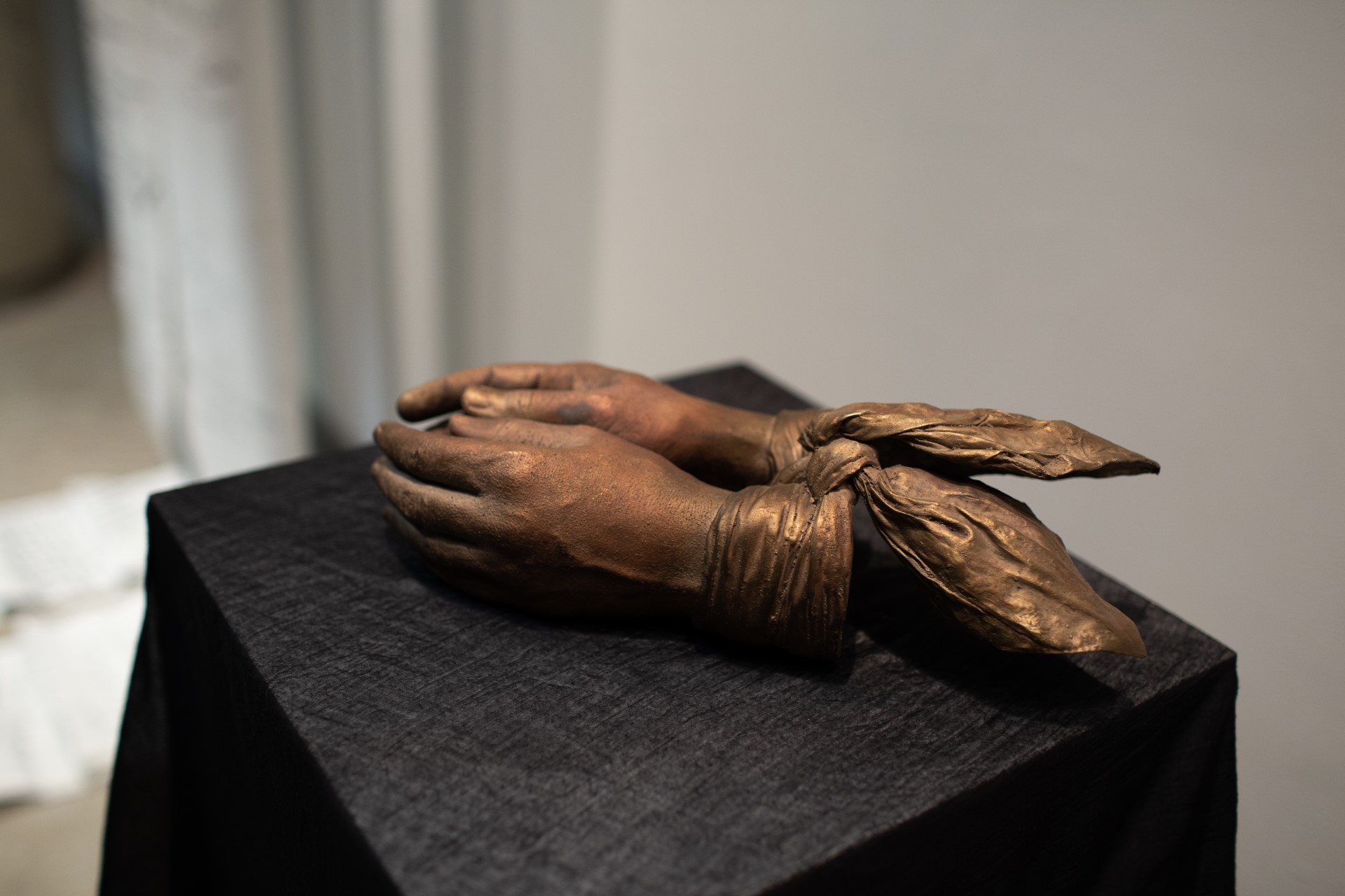 Detailed image of the artist's bronzed casted hands tied with a scarf. 