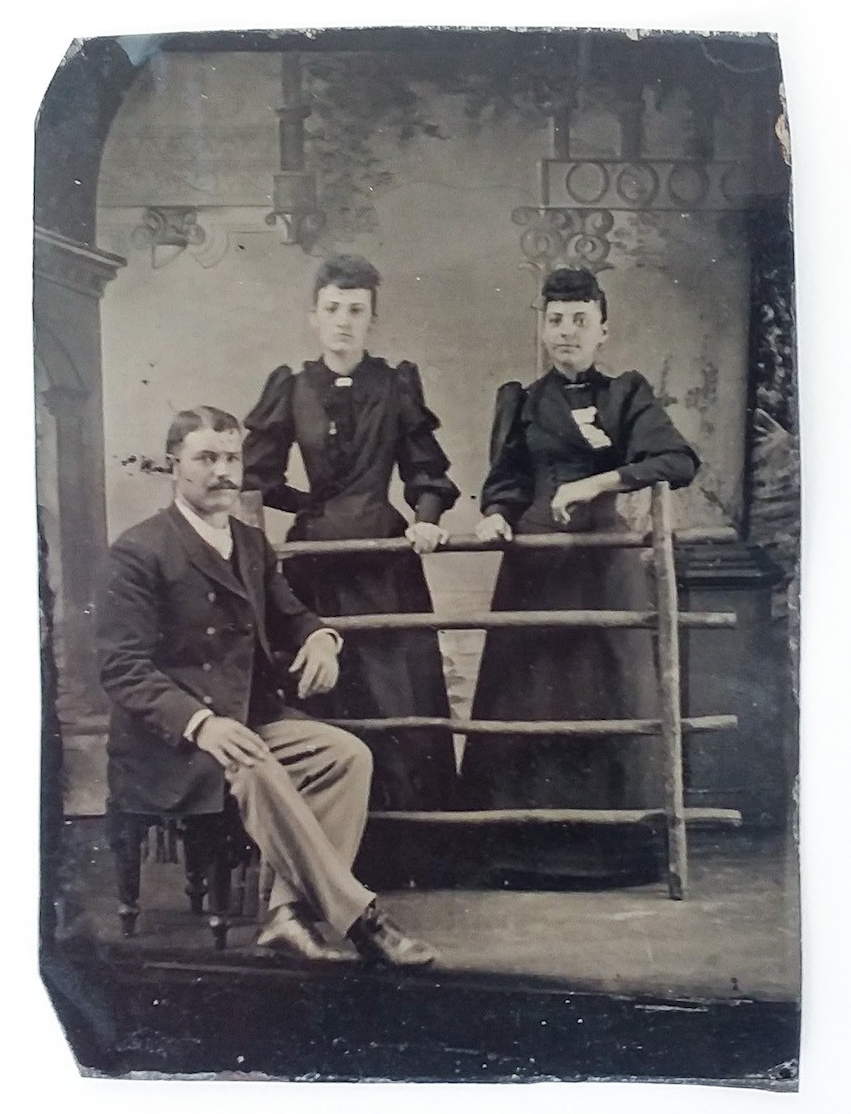 a tintype of two women standing and a man sitting