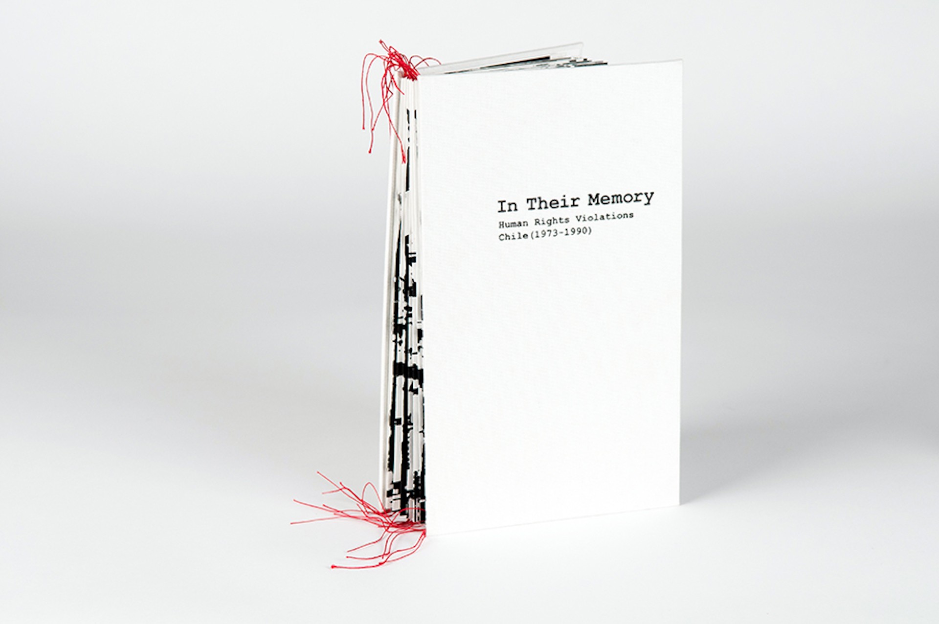 A printed book standing upright with bright red thread emerging from the top and bottom of the book spine. The book is titled "In Their Memory: Human Rights Violations Chile (1973-1990)"