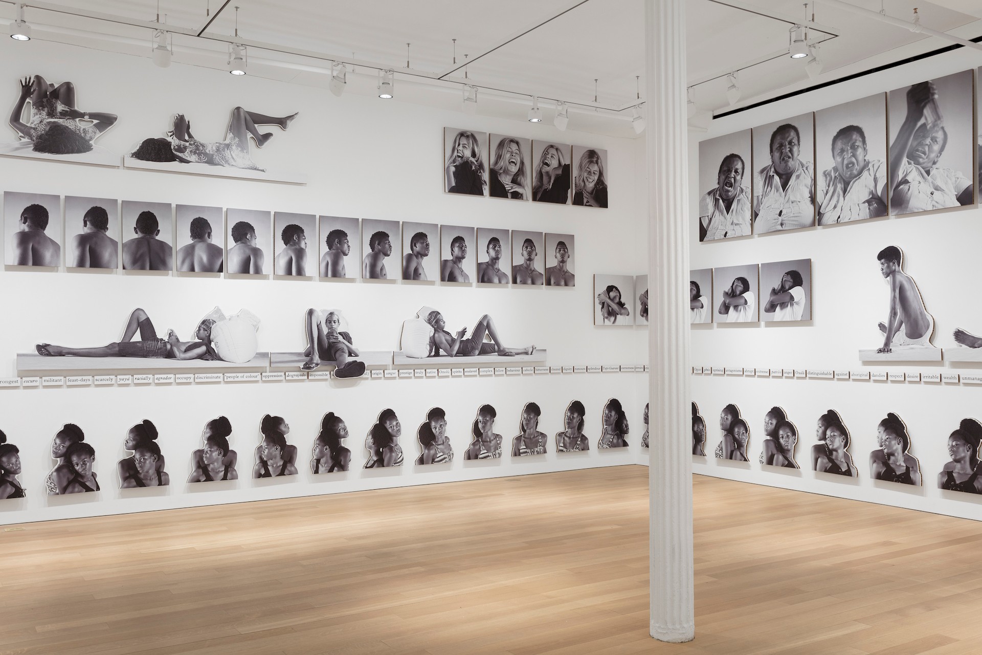 An exhibition space with white walls and light wooden floors with many black and white photographs on the wall for Jonathas de Andrade's project called, "Eu, mestiço."
