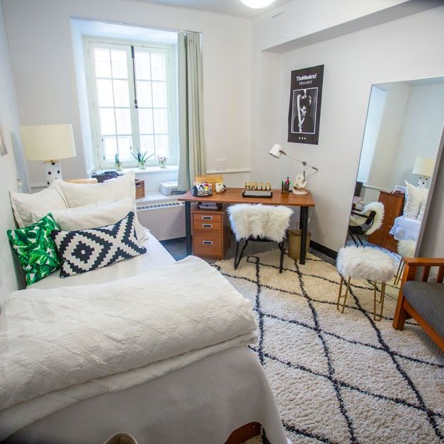 A cozy furnished bedroom in the Grey Nuns residence with a desk in the corner by a large window A cozy furnished bedroom in the Grey Nuns residence with a desk in the corner by a large window
