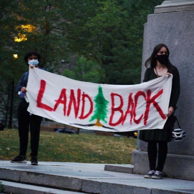 Une photographie de deux manifestants tenant une bannière « Land Back ».