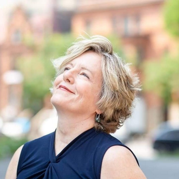 Johanne Pelletier A woman with short blond hair, wearing a sleeveless black top, is looking up toward the sky and smiling