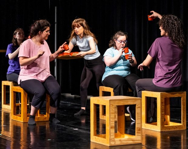 A spotlight on inclusion and accessibility in the arts Five individuals sit on wooden seats on a stage, acting out a scene