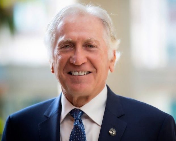 Morton Minc A headshot of a man with white hair is smiling and wearing a dark blue blazer over a white dress shirt and patterned blue tie