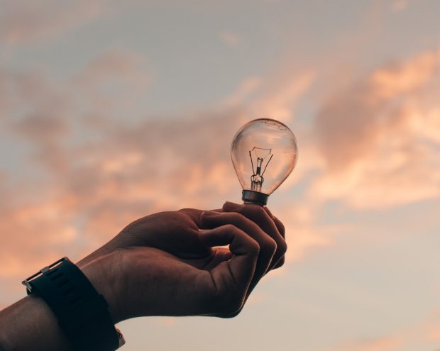 light bulb picture of a hand holding up a light bulb, with sky in the background