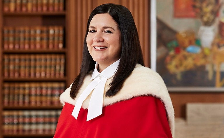 Headshot of jurist standing in front of a painting and bookcase