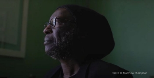 Image of a man with glasses looking sideways against a dark green background