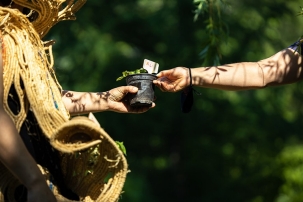 A photo of two people outside against a leafy background passing a potted plant between them.