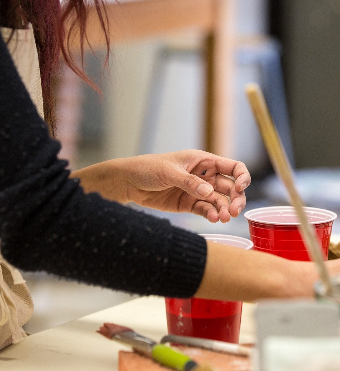 A person painting on top of a table, with several paintbrushes and red solo cups around them