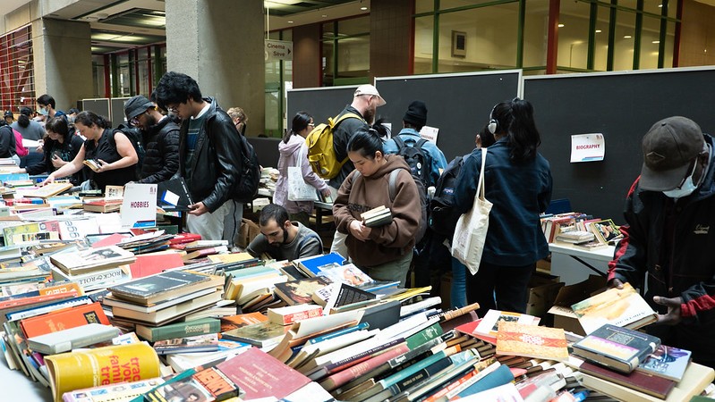 A crowd of people look at and select books from tables set up in an atrium