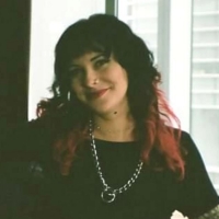 woman with dark, curly hair, wearing black top and large, silver chain