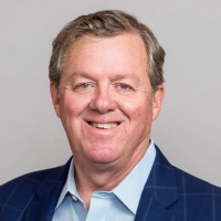 smiling man wearing a button-up shirt and blue jacket looks at the camera