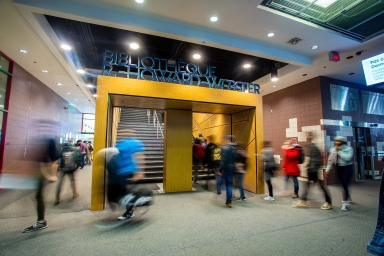 Students come and go in front of the stairs leading up to the library