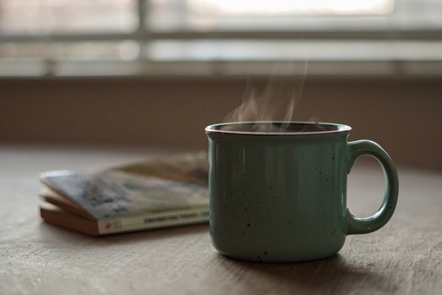 Green mug on a table with steam rising from it.