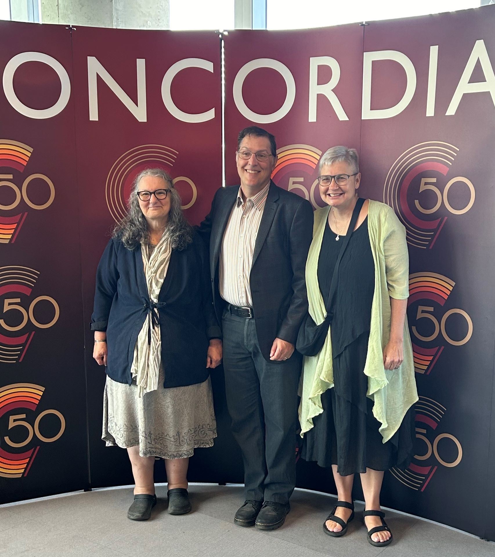 Three adults smiling in front of large maroon background that says Concordia on it.