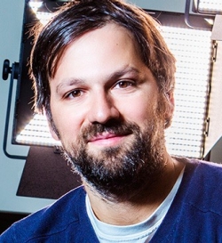 A man with short, dark hair and a beard, smiling