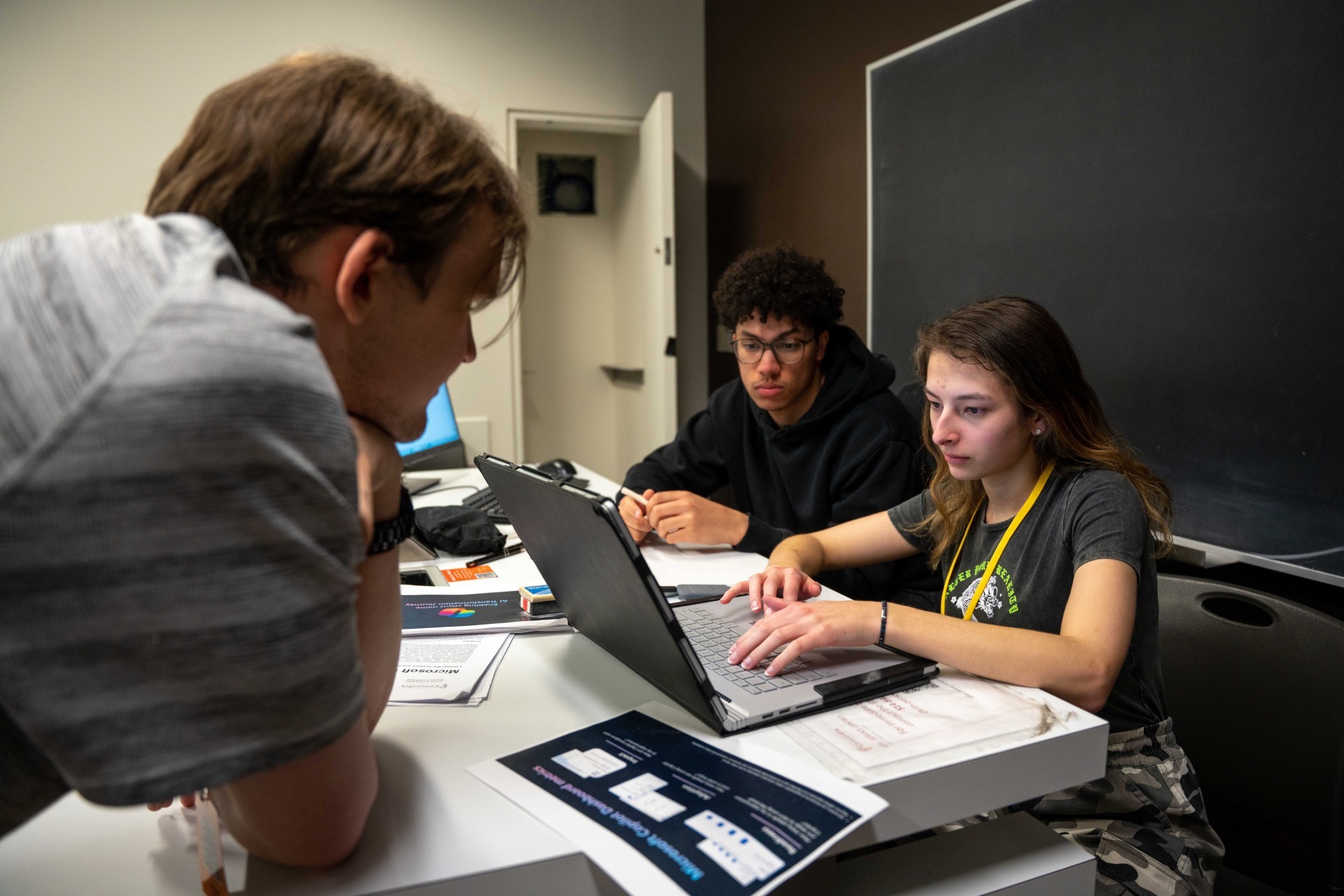 Students collaborating on a cybersecurity challenge, with one working on a laptop while others observe closely in a classroom setting.