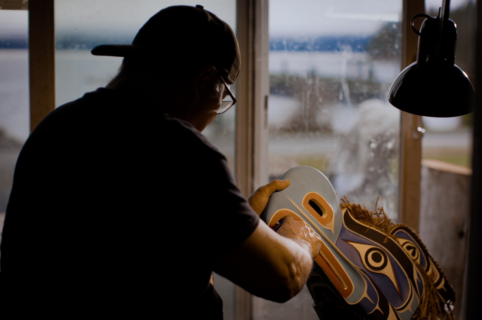 Film still  showing man from behind working on wood in half-light.