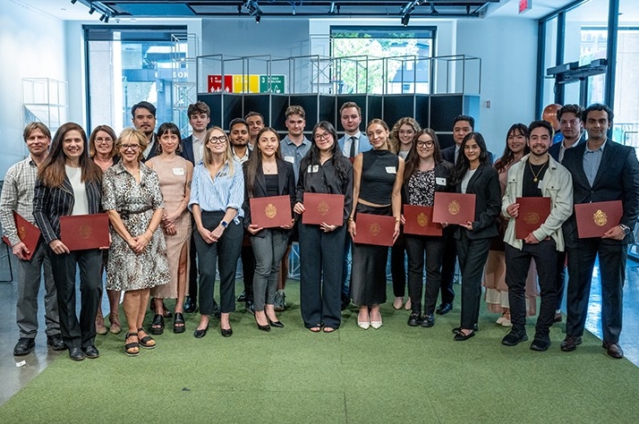 A large group of diverse people in an interior space, standing together, with the front row holding certificates.