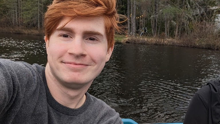 Smiling young man with short, red hair, on a boat with a river in the background