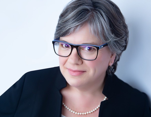 Pascale Sicotte Portrait of woman with shoulder-length hair wearing a black blazer, glasses and a pearl necklace