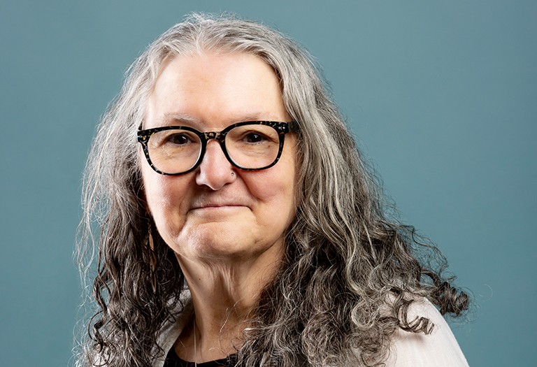 Smiling woman with ling, greying hair and wearing glasses