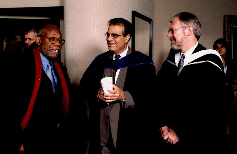 Three smiling people in university graduation regalia