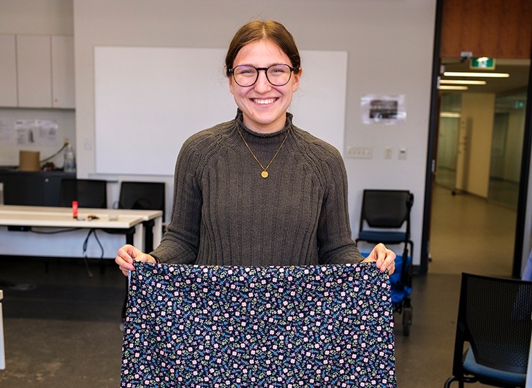 Smiling young woman with long hair and glasses holding up a patterned piece of fabric.