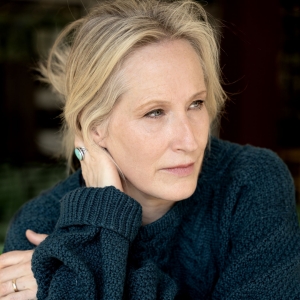 Woman wearing a dark sweater, gazes thoughtfully into the distance.