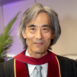 Man with long salt and pepper hair smiles into the camera wearing graduation gown.