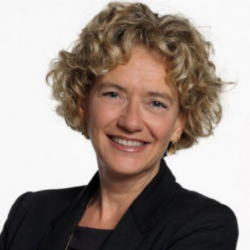Woman with curly blond hair wearing black jacket smiles into the camera.