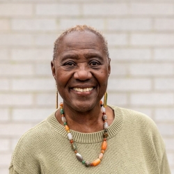 A woman with a green sweater and colorful jewelry smiles into the camera.