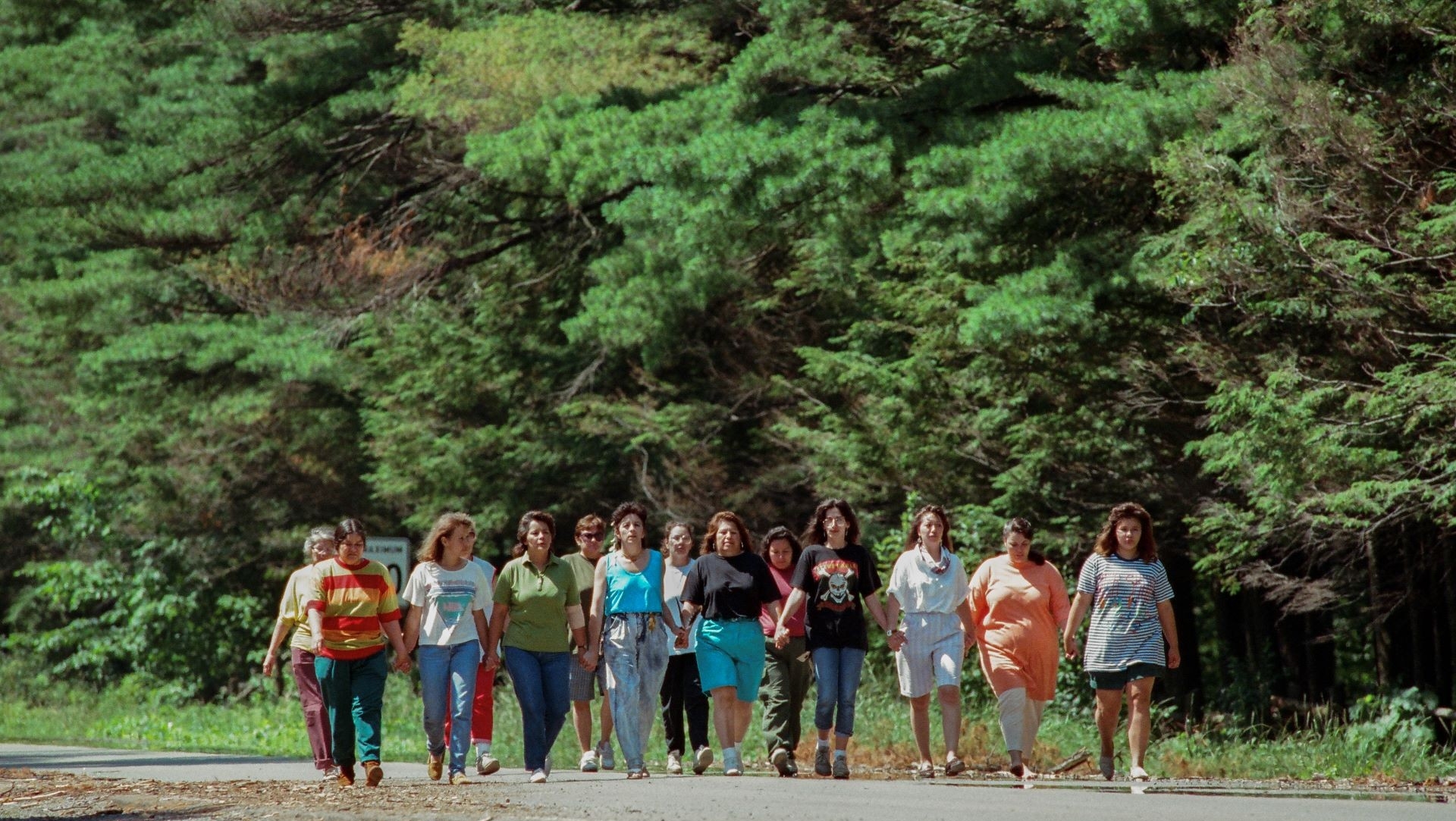 A group of women walking together on a road surrounded by trees.