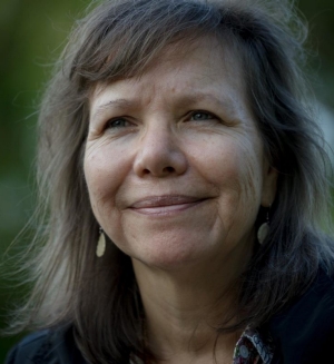 Portrait of a woman with shoulder-length hair smiling in front of a blurred green background