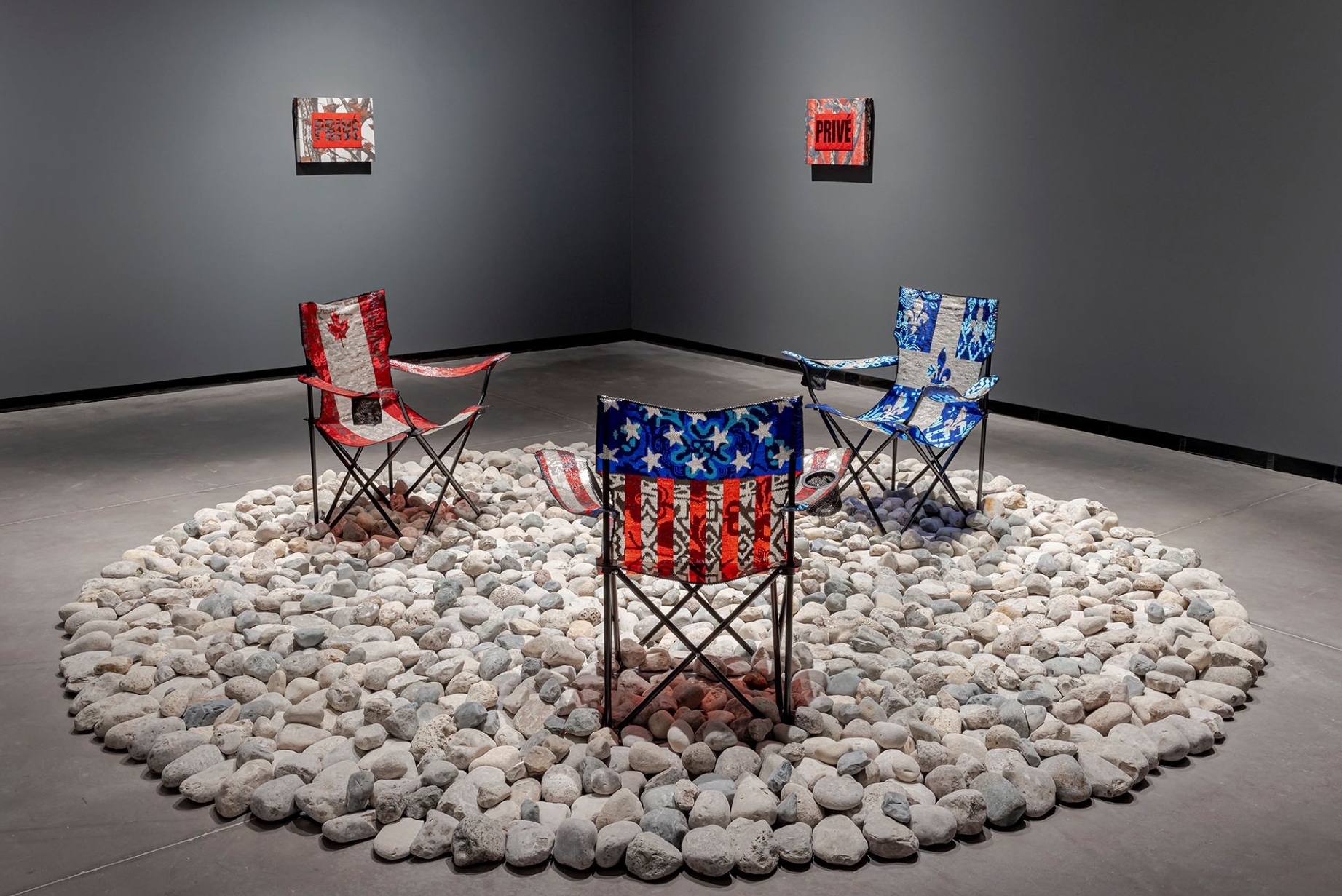 An art installation featuring folding chairs decorated with beadwork, placed in a circle on a bed of rocks.