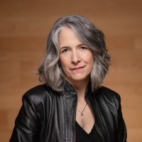 A woman with grey hair wearing a leather jacket sits for a portrait.