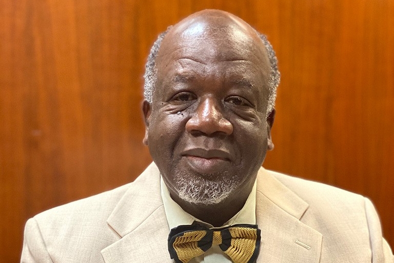 Patrick wears a cream suit jacket over a light yellow shirt with a knitted bowtie.