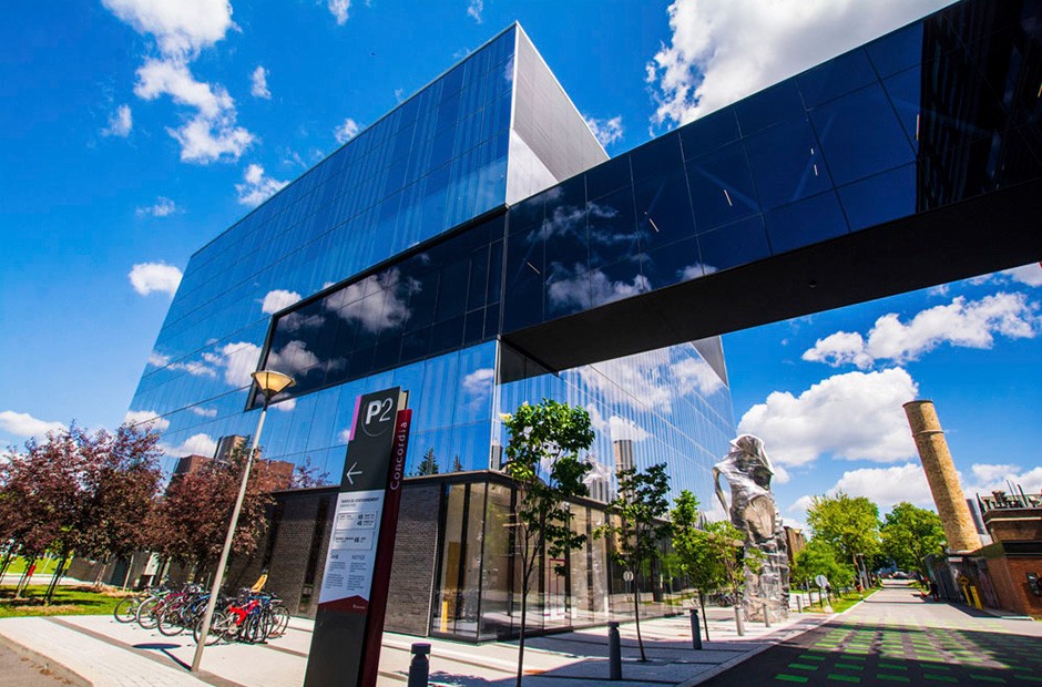 A modern shiny buidling with mirrored walls reflects a blue sky above and trees and grass below