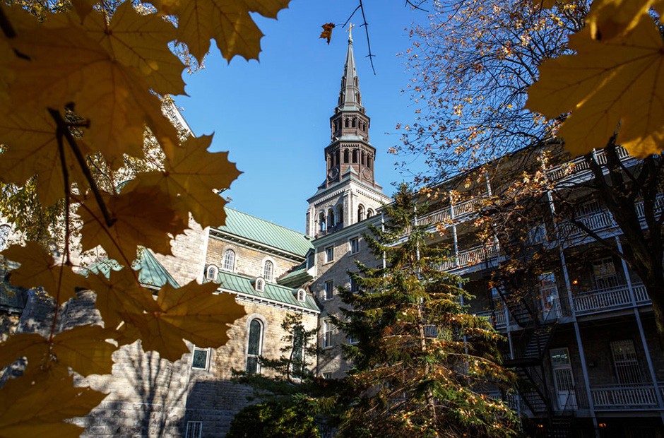 The spire of the Grey Nuns chapel is seen from below against a blue sky and is surrounded by autumn leaves