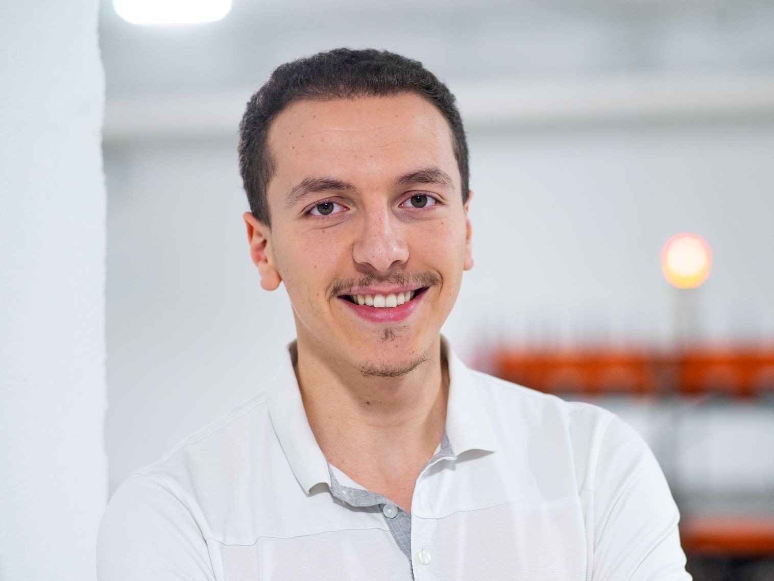 A man in a white button down polo shirt smiles with his arms crossed.