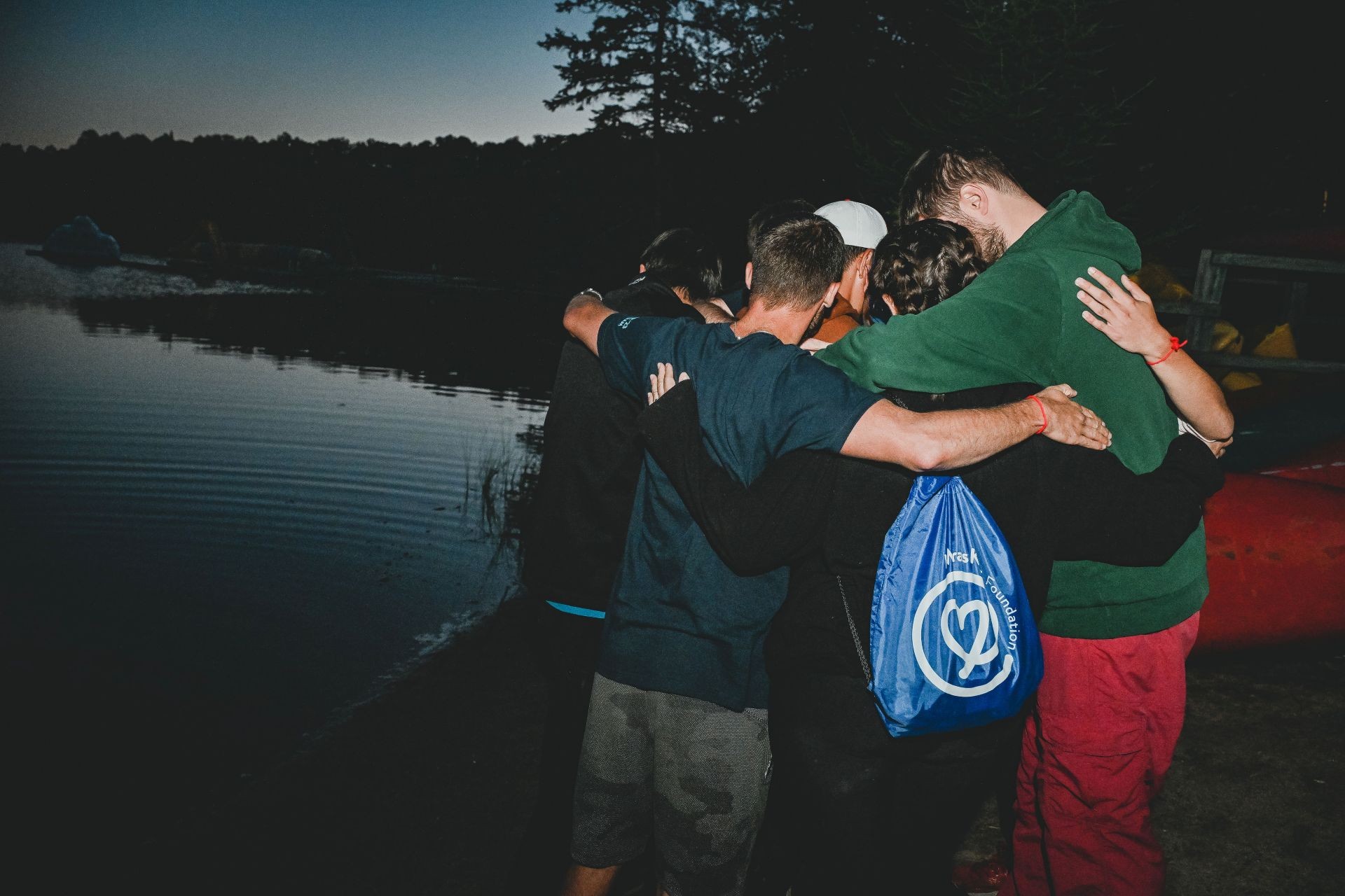 A group of kids stand huddled in front of a lake at dusk